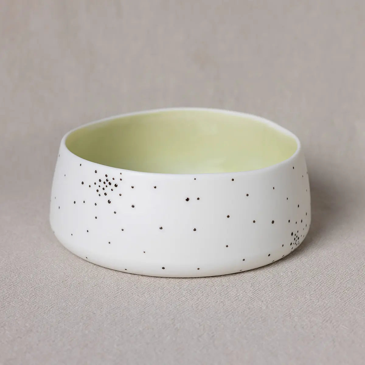 A Breda Bowl, dotty by Urchic Porcelain, with small black dots and a light yellow interior is placed on a beige surface.