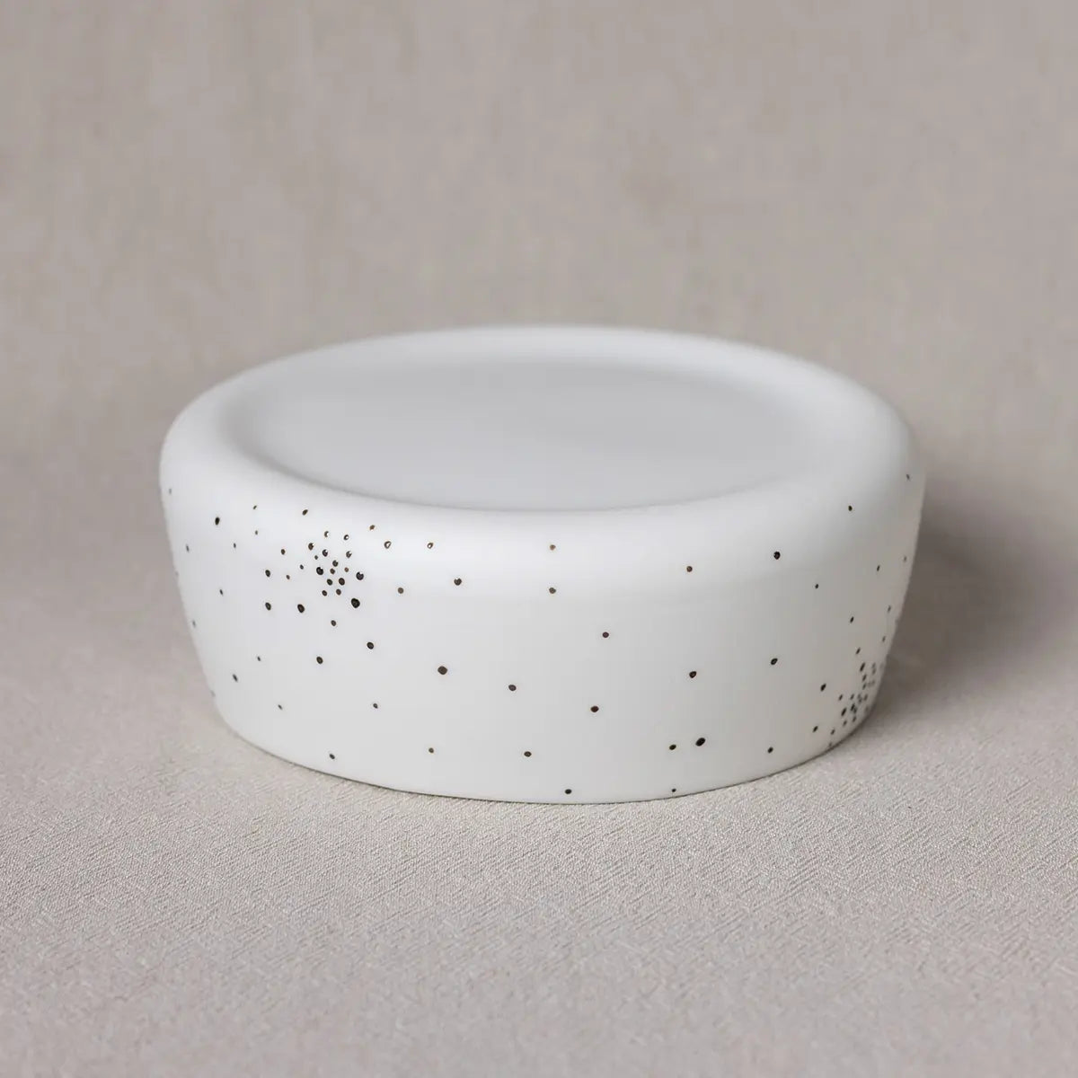 The Breda Bowl, dotty by Urchic Porcelain is a white, round ceramic container with a fitted lid, featuring small black speckles scattered across its surface. This decorative piece adds a touch of elegance and sophistication to any setting.