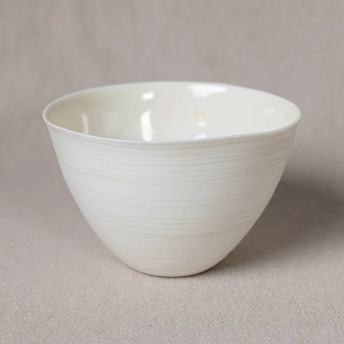 A versatile piece of porcelain dinnerware, the Urchic Porcelain Martinka Bowl with lines features a smooth matte finish and slight horizontal ridges, elegantly placed on a light beige surface.