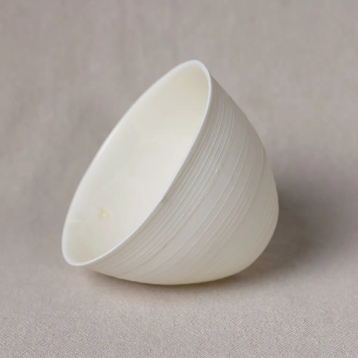 A Urchic Porcelain Martinka Bowl with lines, featuring a white, smooth finish and subtle horizontal ridges, is displayed tilted sideways on a plain background. This versatile piece adds understated elegance to any setting.