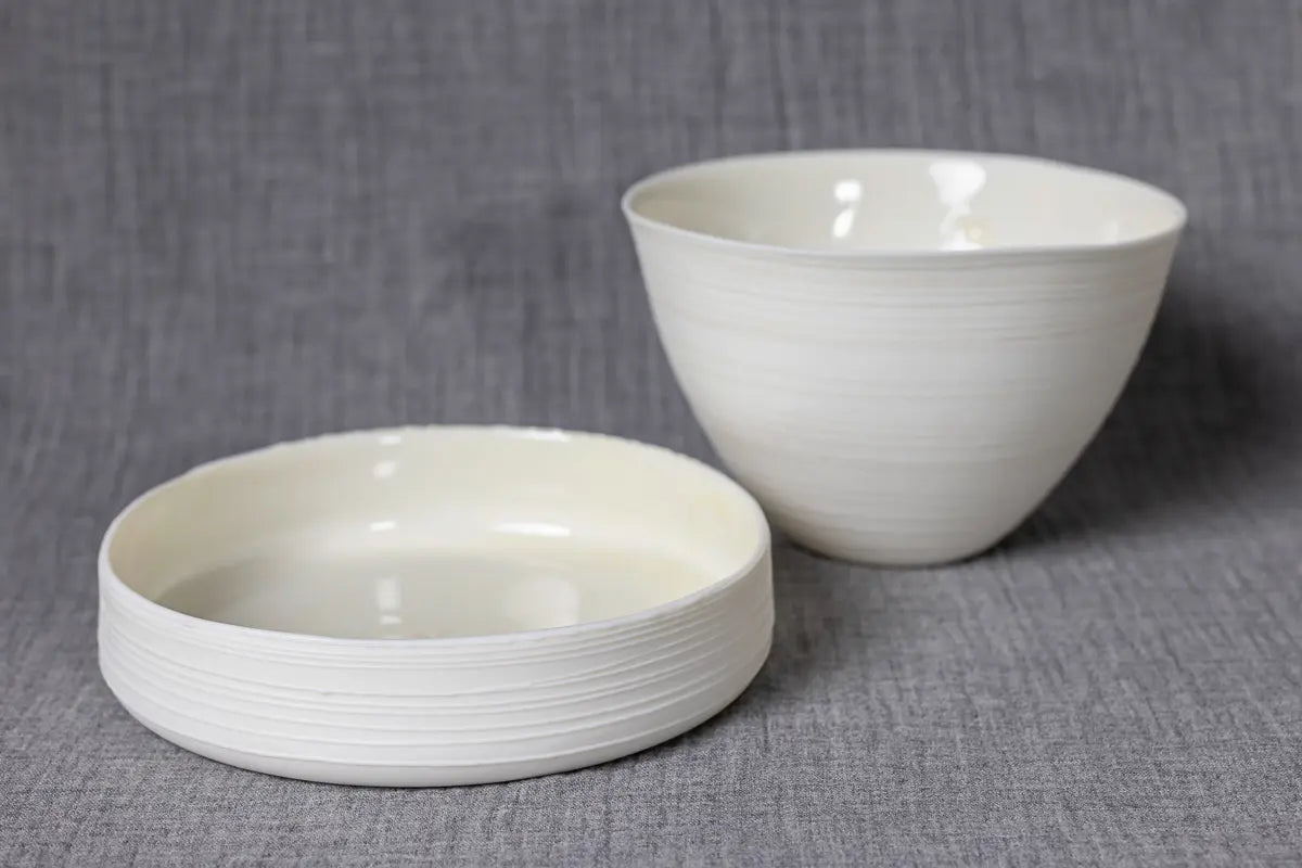 A Breda Mini Bowl with lines by Urchic Porcelain is placed on a gray fabric background, creating an elegant decorative piece.