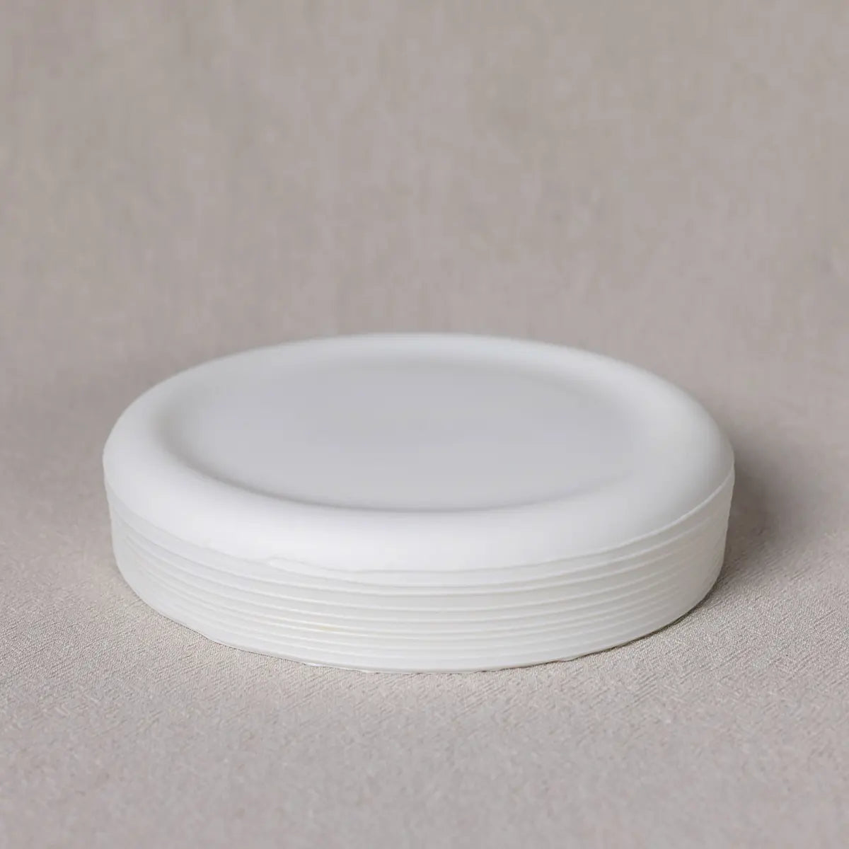 A stack of white, round, plastic lids is placed on a light beige surface, subtly echoing the elegance of the Urchic Porcelain Breda Mini Bowl with lines.