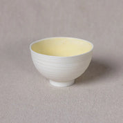 The Vida Bowl by Urchic Porcelain, a small white ceramic bowl with a light yellow interior that exudes timeless elegance, is placed on a neutral-colored surface.