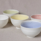 Five Vida Bowls from Urchic Porcelain in pastel hues (white, green, yellow, pink, and blue), arranged on a neutral surface, radiate timeless elegance.