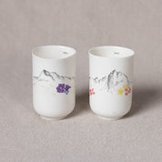 Two cups from the Urchic Porcelain Soulmates Set, titled "Summit Serenity" and "Peak Peace," feature minimalist mountain designs and flower patterns, resting on a light textured surface. Each handmade cup has distinct numbers printed on top: "2864" and "2645," inspired by Slovenian mountain ranges.