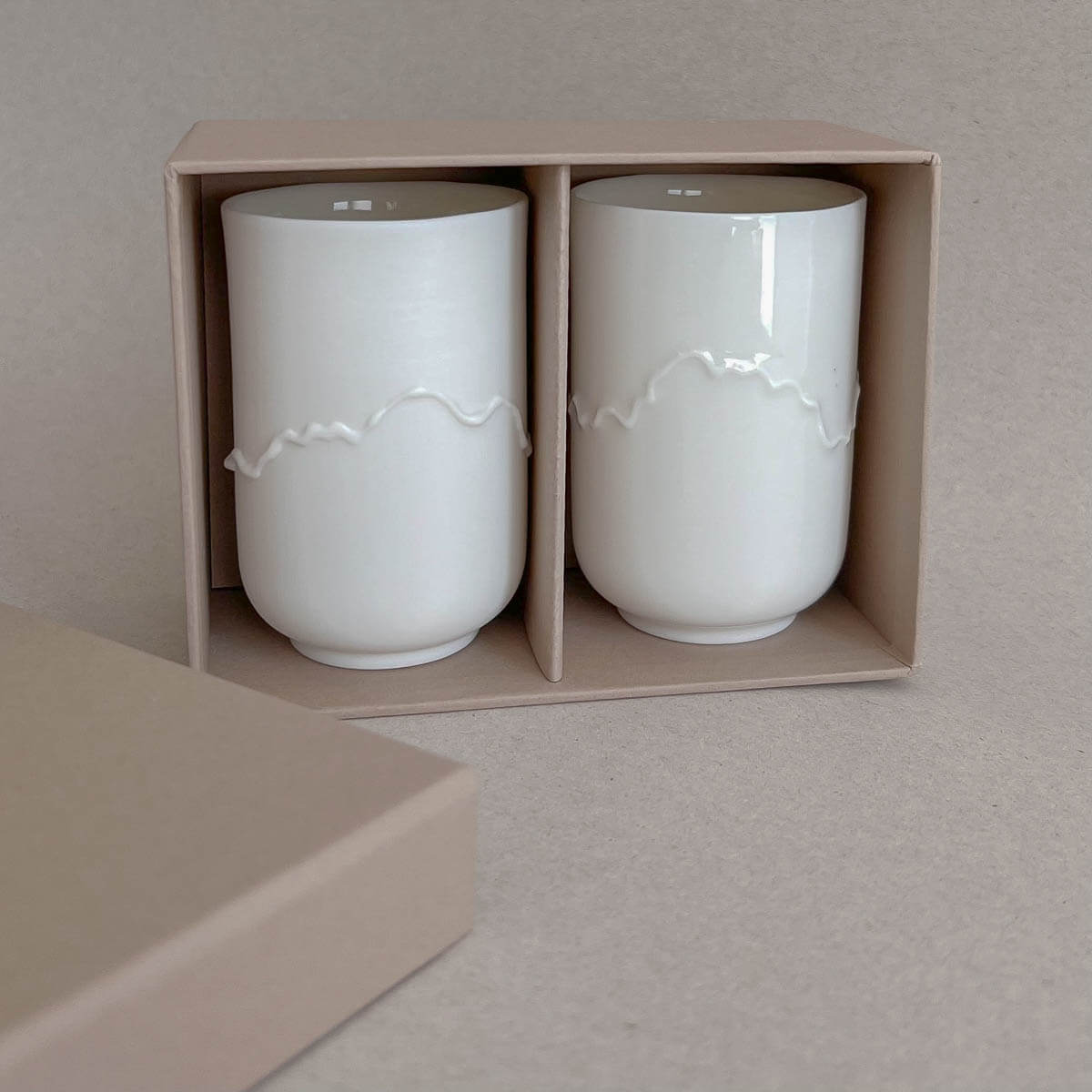 The Soulmates Cup Set of Two Cups, Alpine Poetry from Urchic Porcelain features a pair of handmade porcelain coffee cups with a wavy design in the middle and comes elegantly packaged in a beige box. Made in Slovenia, this exquisite set takes inspiration from the Slovenian mountain ranges.