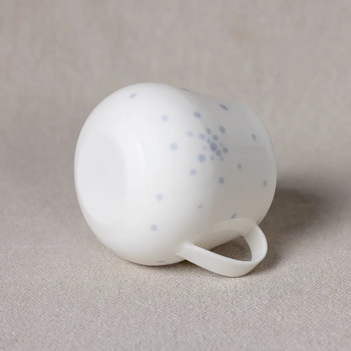 The Nova Cup from Urchic Porcelain, featuring a blue dots pattern, lying on its side on a beige surface.