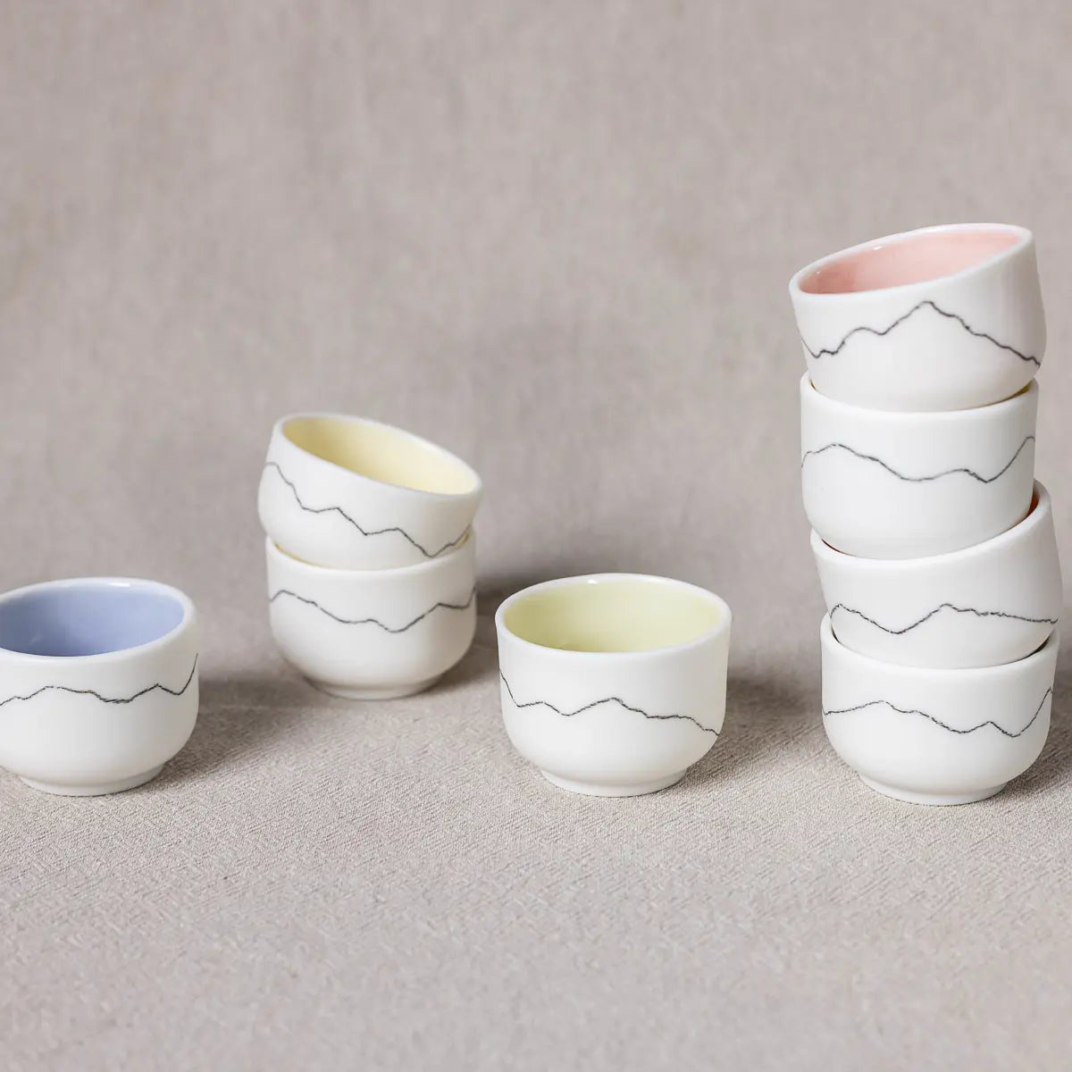 The Kiki mini set of four cups from Urchic Porcelain, featuring a charming mountain-like line design around the exterior, comes in a collection of colorful cups. Some are stacked while others are placed separately, and each mini ristretto cup boasts interiors in soothing pastel shades.