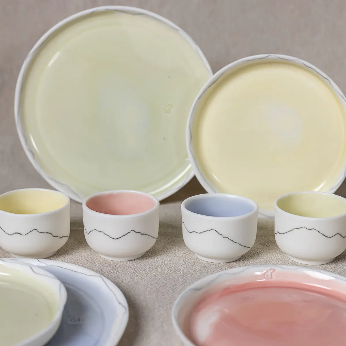 A collection of the Kiki mini set of four cups by Urchic Porcelain, featuring ceramic pieces in pastel shades of yellow, pink, blue, and white, arranged neatly on a beige surface.