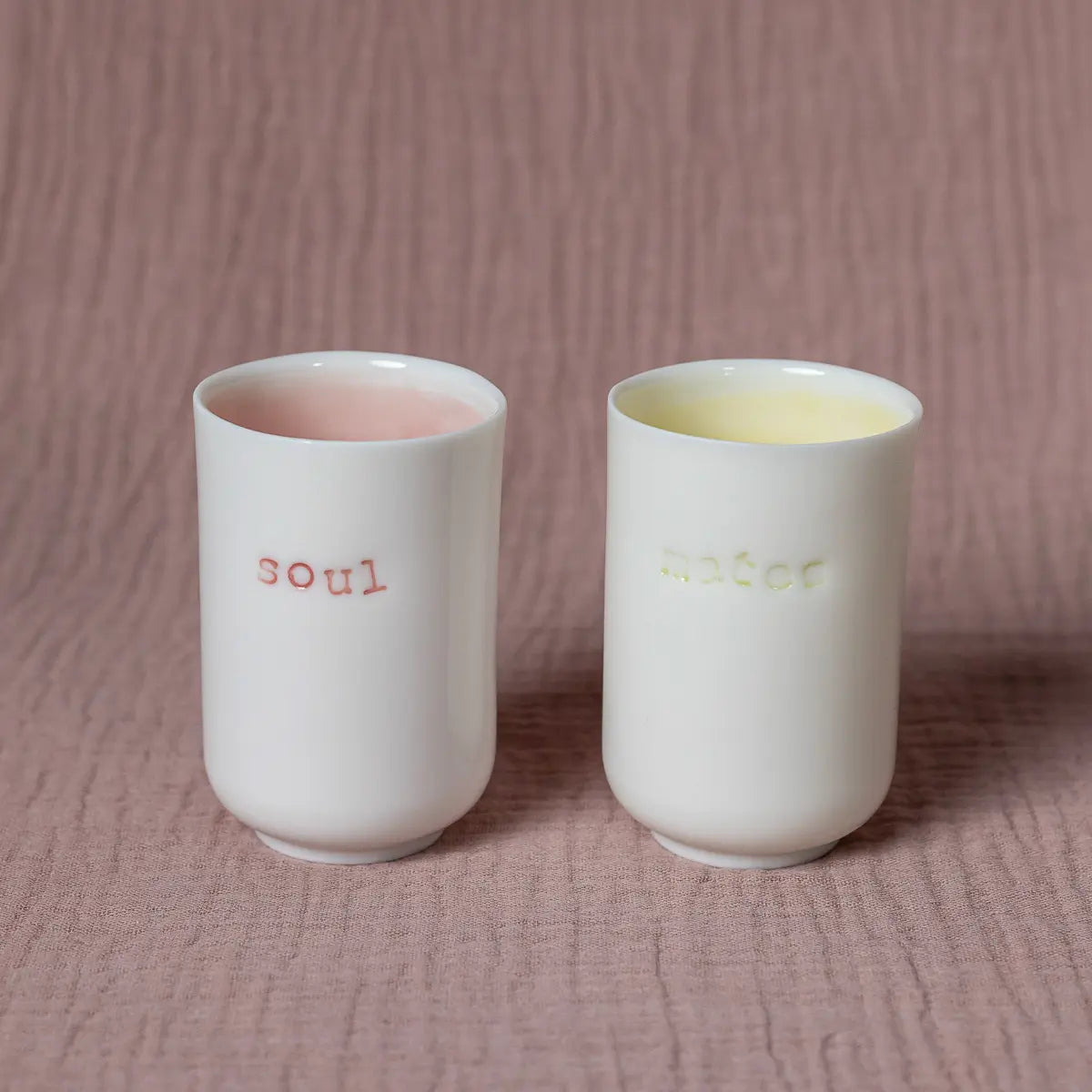 Presenting the Urchic Porcelain Soulmates coffee set, a minimalist collection featuring two white porcelain cups elegantly displayed on a textured surface. One cup bears the word "soul" inscribed in pink, while the other showcases "mate" in yellow, making it the ideal Soulmates coffee set.