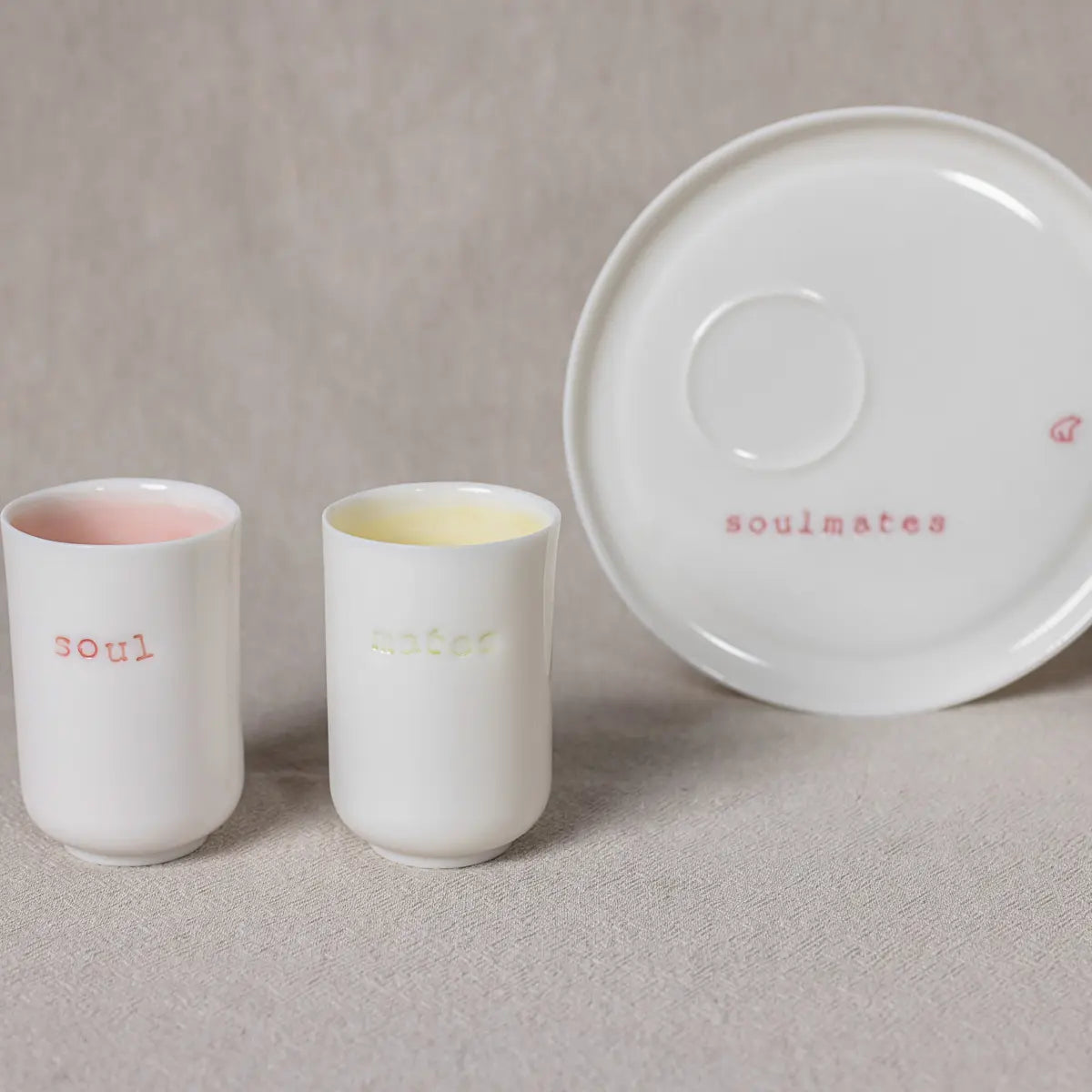 The Soulmates Porcelain Coffee Set by Urchic Porcelain is a minimalist and elegant addition to any home. This exquisite set features two white porcelain cups, each inscribed with "soul" and "mate," along with a matching white saucer labeled "soulmates." Perfectly capturing the essence of togetherness, this set is ideal for those special shared moments.