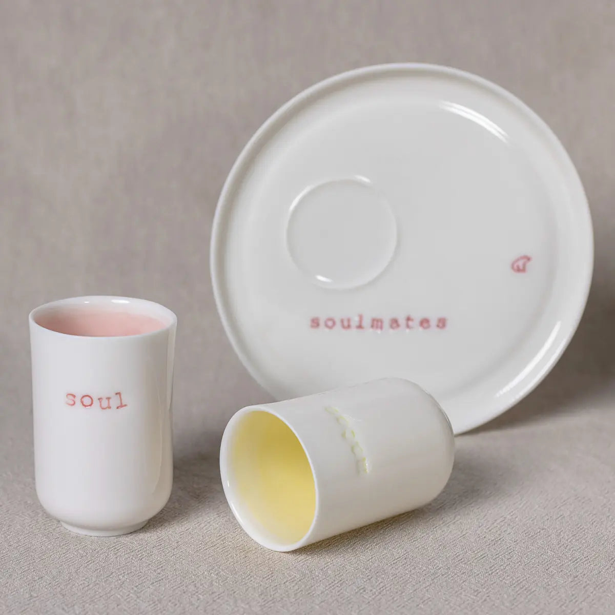 Introducing the Soulmates porcelain coffee set by Urchic Porcelain: a chic set featuring two minimalist cups. One labeled "soul" boasts a pink interior, while the other cup, simply adorned with a yellow interior. Great for those intimate mornings together.