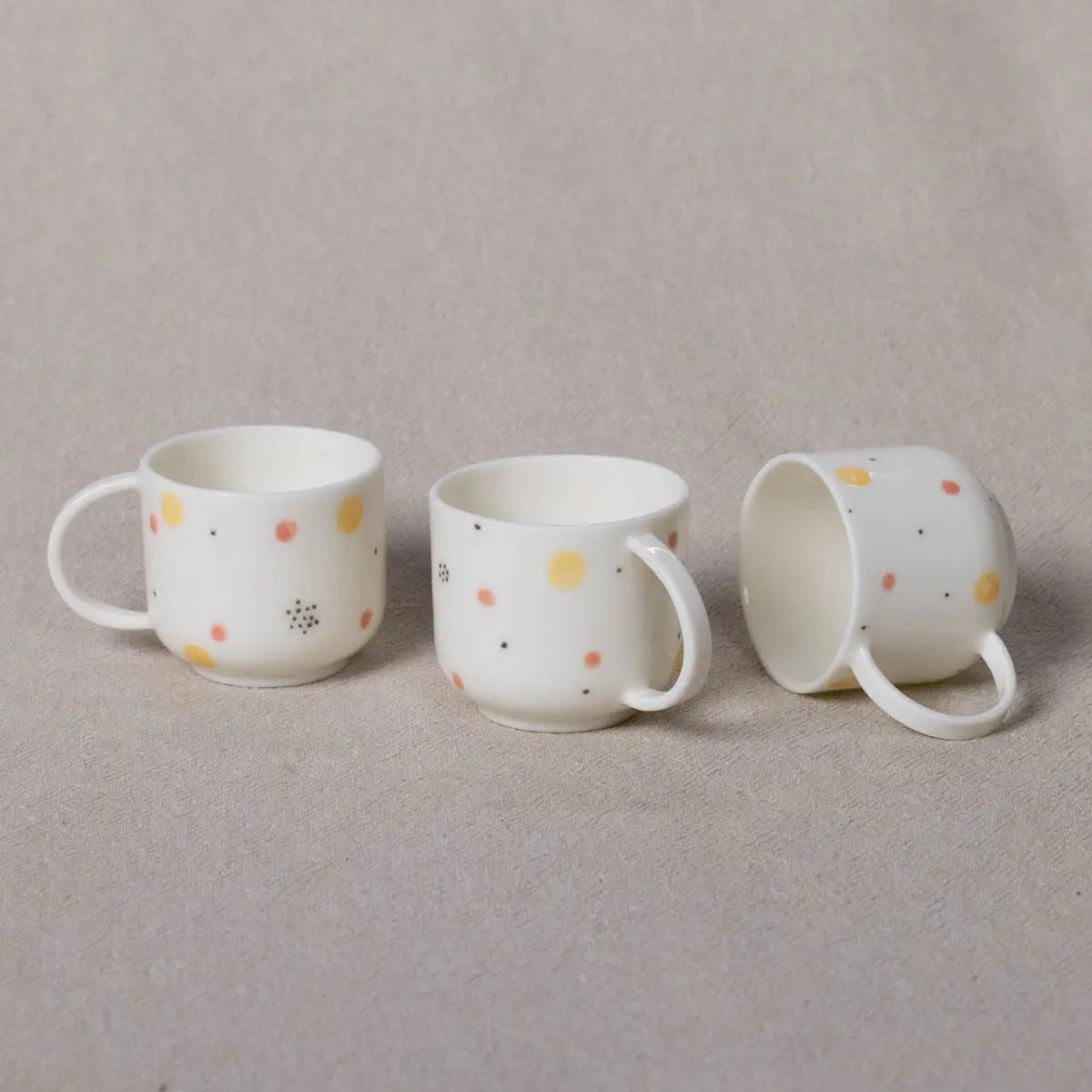 Three Urchic Porcelain Espresso Mini Cups, styled with the vibrant Fireworks pattern, are arranged on a light-colored fabric, with one cup lying on its side—perfect for those special coffee moments.