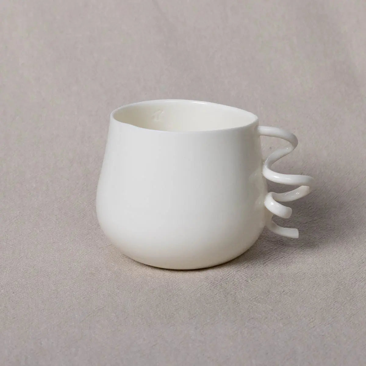 The Nova Cup SPECIAL from Urchic Porcelain features a unique curly handle composed of three curved loops, displayed against a plain, light beige background.