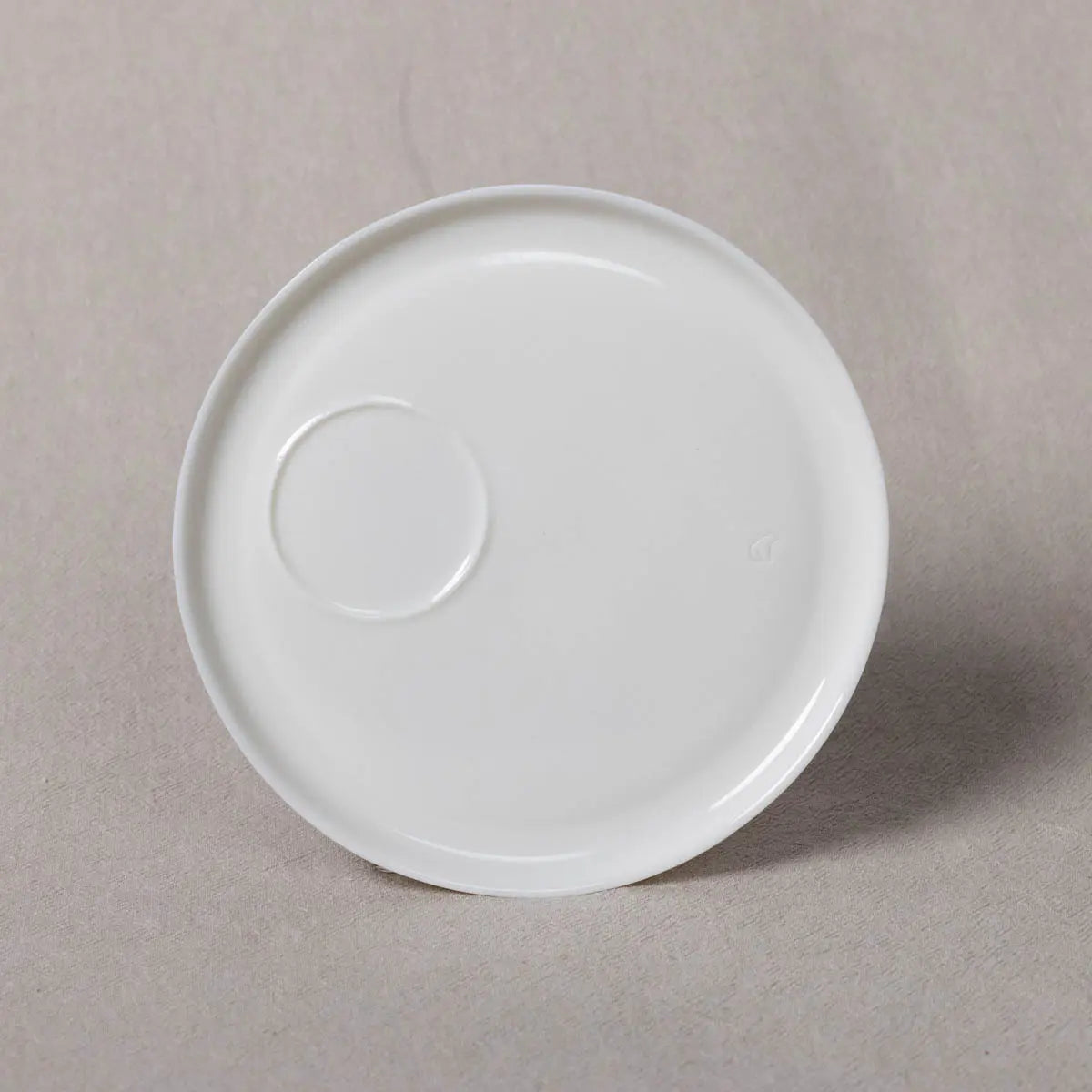 A plain white ceramic Saucer Kiki from Urchic Porcelain, designed specifically for Soulmates Cups, sits on a beige surface, ready to complement your snowy white Kiki cup.