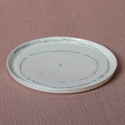 A TRDINKA dinner plate with a Corn fields pattern around the rim, from Urchic Porcelain, placed on a pink textured surface.