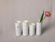 Four white ceramic vases with minimal black dot patterns are lined up on a light beige surface. The tallest vase, an elegant vertical one from Urchic Porcelain's Vase Kiki collection featuring the Blossoms Pattern, holds a single pink tulip as a decorative accent.