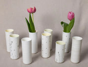 A set of elegant Vase Kiki vases from Urchic Porcelain, featuring sophisticated white ceramic with delicate black flower designs, each holding a single pink tulip and arranged on a neutral fabric background. These decorative accents effortlessly elevate the aesthetic of any space.