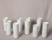 A collection of tall, white ceramic vessels with elegant designs is displayed on a neutral background. Some of these items, branded as Vase Kiki from Urchic Porcelain, feature delicate floral patterns called Blossoms Pattern, while others showcase subtle horizontal ridges or dotted accents for decoration.