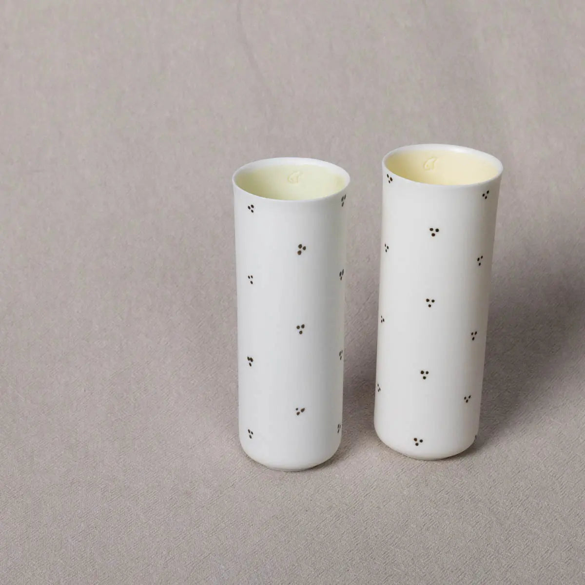 Two elegant vertical vases crafted from translucent porcelain, each adorned with a delicate Blossoms pattern, standing on a light gray surface. These are the Vase Kiki by Urchic Porcelain.