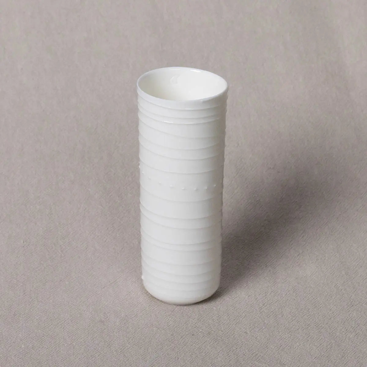 Vase Kiki, Lines Pattern by Urchic Porcelain is a tall, cylindrical white vase with horizontal ridges that serves as an elegant decorative accent on a light gray surface.