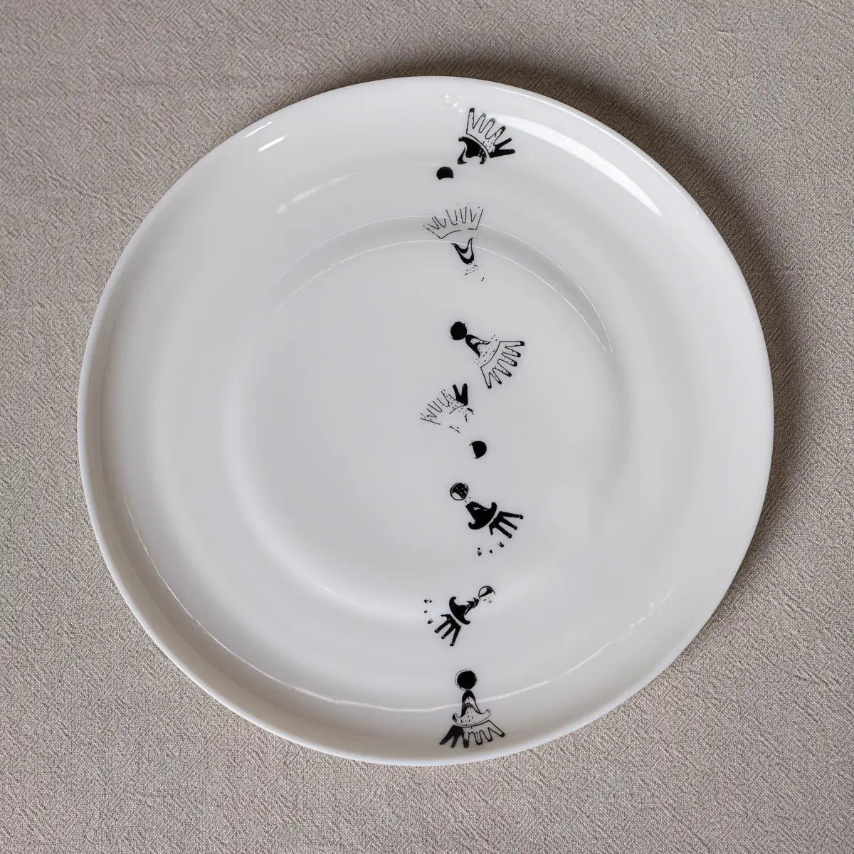 The Vurnik Carnation pattern dinner plate set by Urchic Porcelain features a white plate adorned with small, abstract black bird-like designs arranged along a curved line near the edge. Set on a light grey, textured surface, it perfectly complements your dinnerware collection.