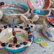 Urchic Porcelain's GLINARIJE NA LONTRGU: Poletna mala šola gline za otroke - AKONTACIJA features handmade ceramic bowls and a painted rabbit, showcasing children's creativity and enhancing fine motor skills through hands-on clay activities.
