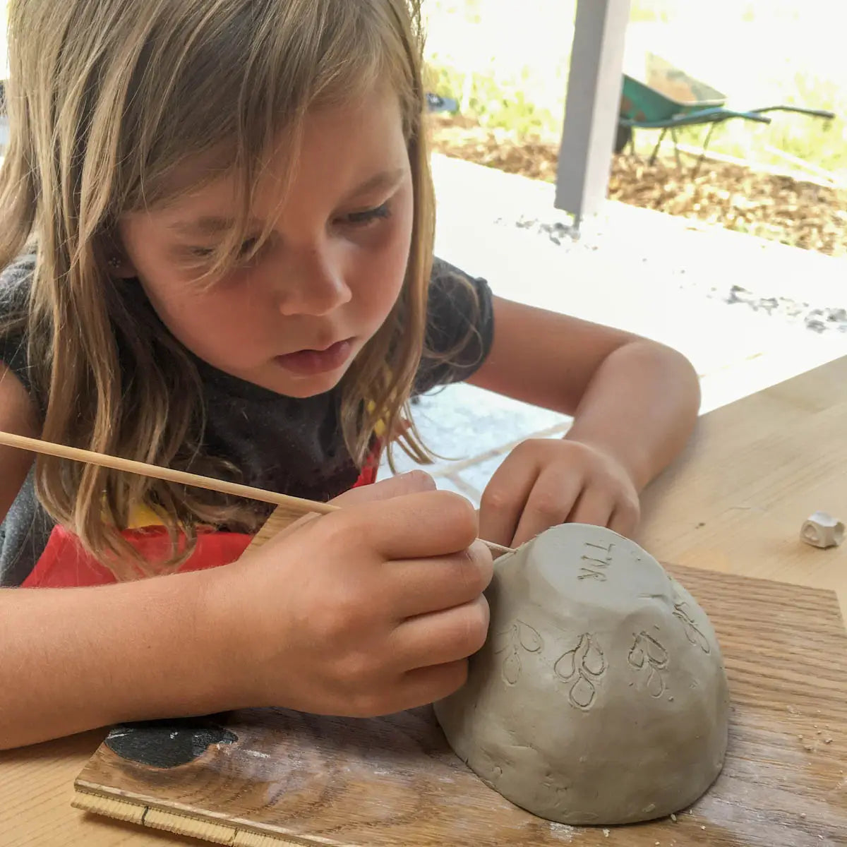 At Urchic Porcelain's GLINARIJE NA LONTRGU: Poletna mala šola gline za otroke – AKONTACIJA, children use wooden tools to shape clay on boards, boosting creativity and fine motor skills at a fun summer pottery workshop.