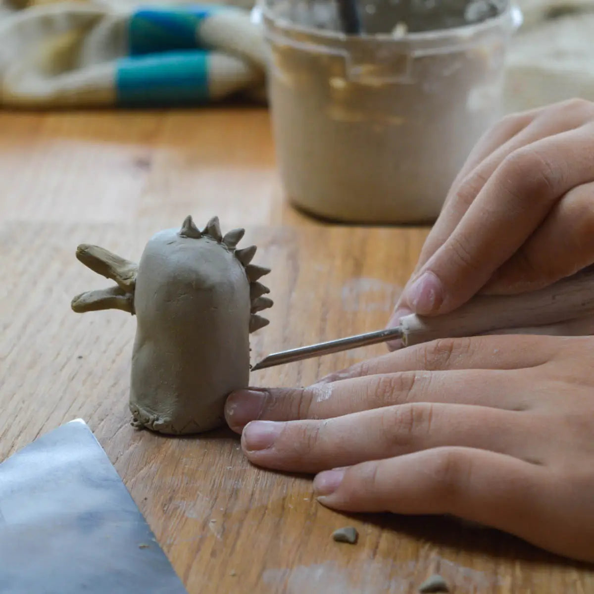 A child explores creativity and fine motor skills at Urchic Porcelain's "GLINARIJE NA LONTRGU: Poletna mala šola gline za otroke - AKONTACIJA," shaping unique clay sculptures.
