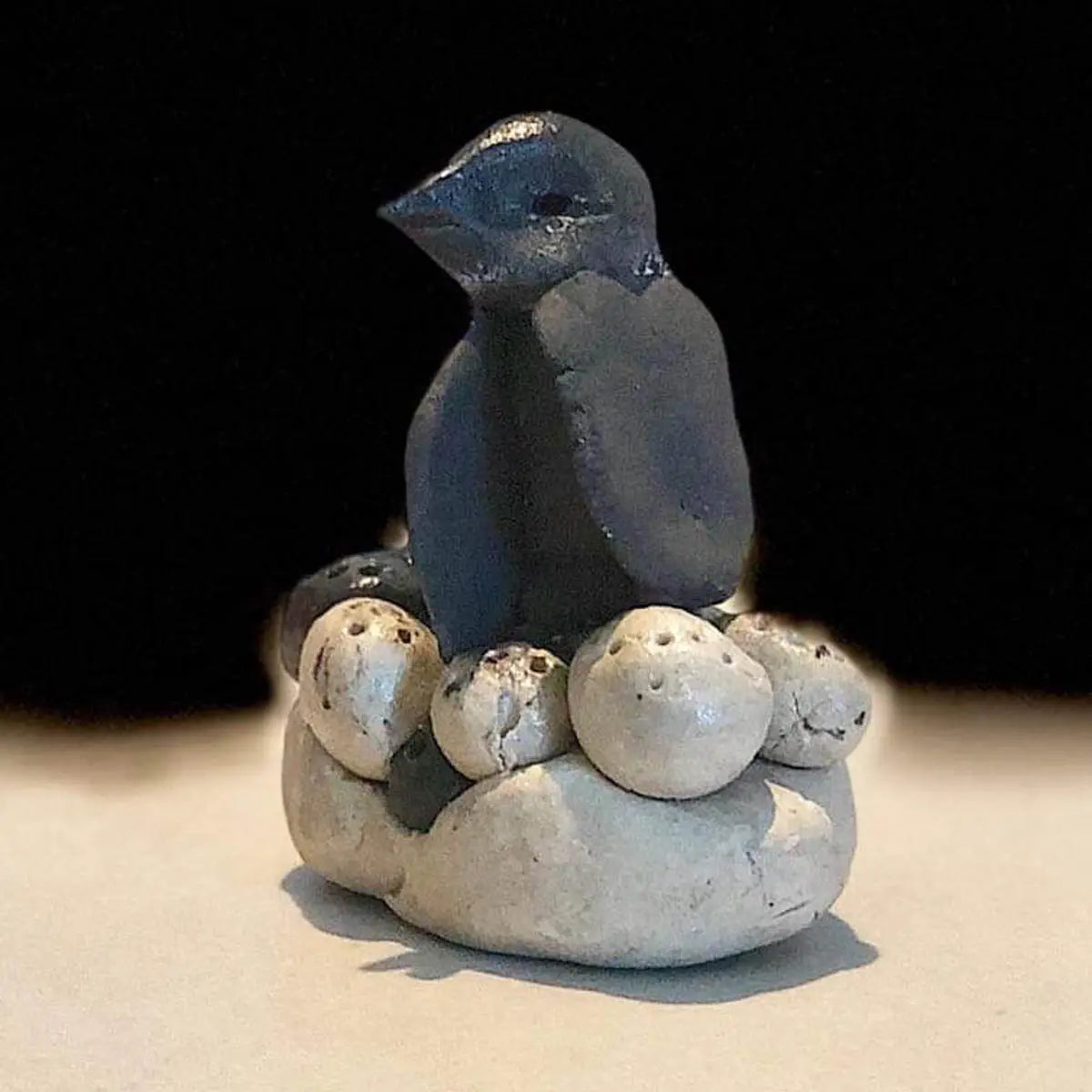 Urchic Porcelain’s "GLINARIJE NA LONTRGU: Poletna mala šola gline za otroke - AKONTACIJA" features a dark bird sculpture on a nest of white eggs and stones, displaying children’s creative skills on a plain background.