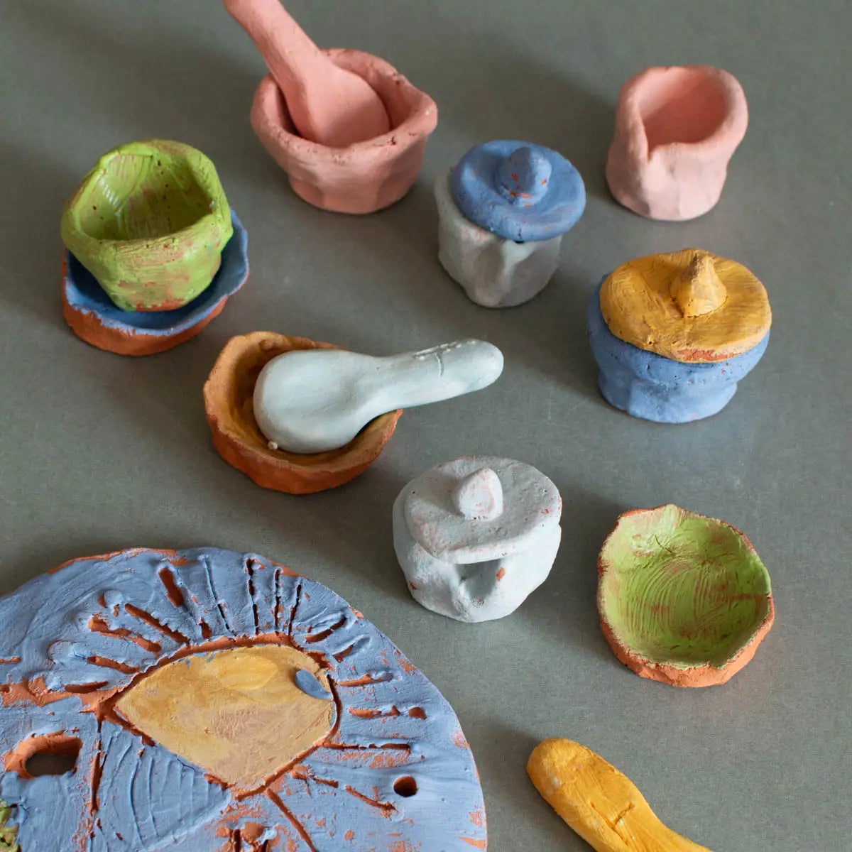 Urchic Porcelain's GLINARIJE NA LONTRGU: Poletna mala šola gline za otroke - AKONTACIJA features pastel clay bowls, plates, and tools—perfect for nurturing children's creativity at a summer pottery workshop.