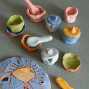Urchic Porcelain's GLINARIJE NA LONTRGU: Poletna mala šola gline za otroke - AKONTACIJA features pastel clay bowls, plates, and tools—perfect for nurturing children's creativity at a summer pottery workshop.