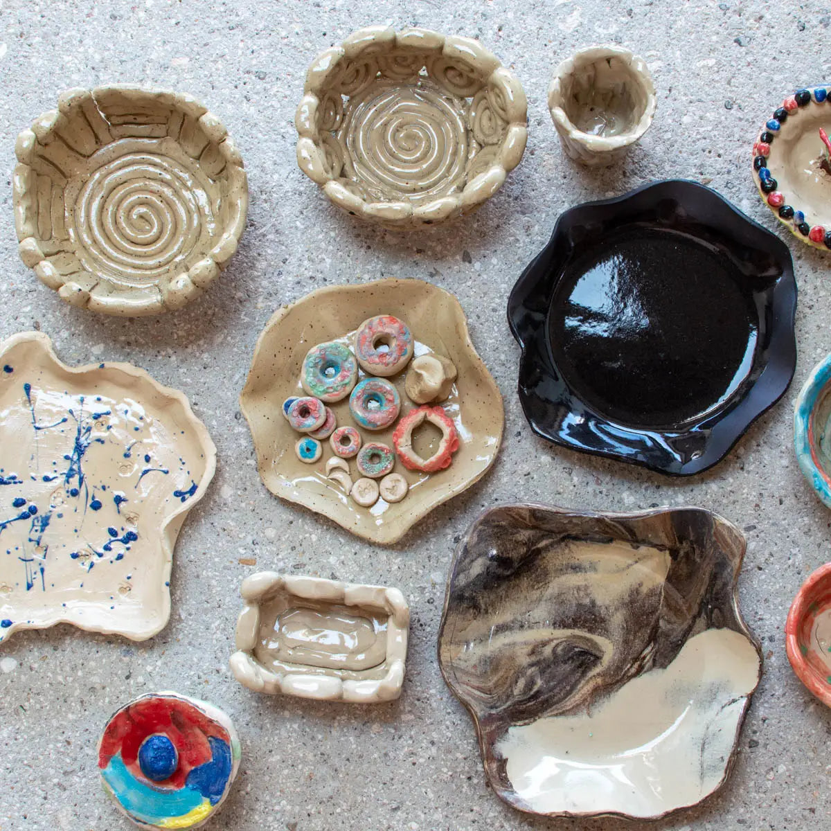 Urchic Porcelain’s GLINARIJE NA LONTRGU: Poletna mala šola gline za otroke - AKONTACIJA features assorted handmade ceramics—ideal for sparking children’s creativity or for displaying creations from a summer pottery workshop.
